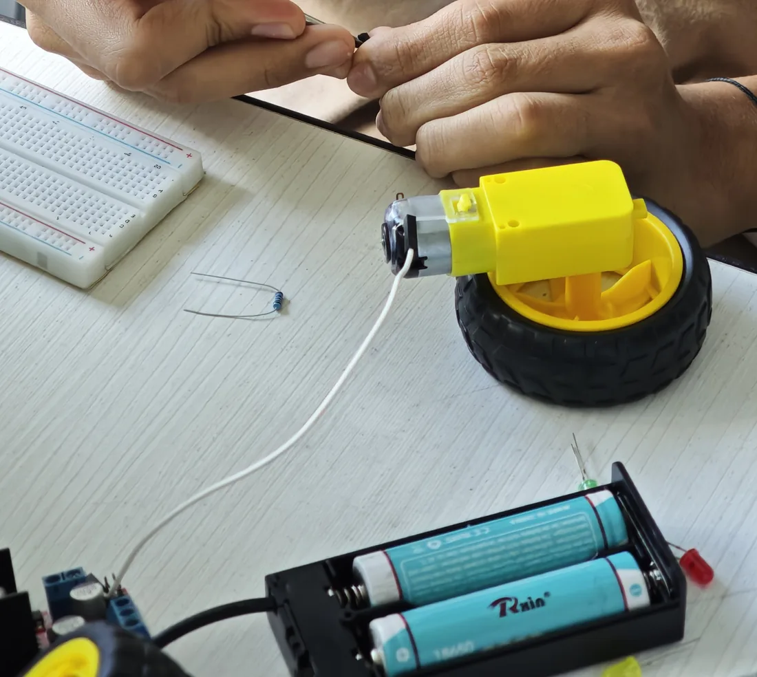 Estudiante arma un circuito con motor, rueda, protoboard y baterías
