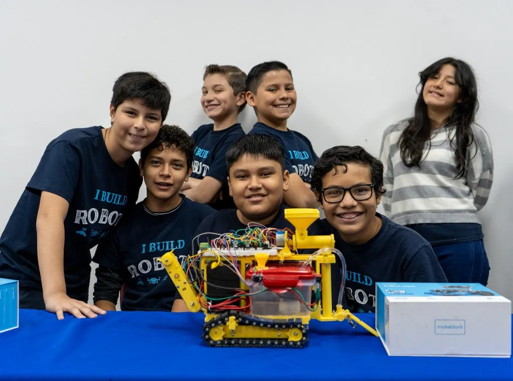 Estudiantes sonríen detrás del robot que construyeron juntos